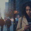 Professional woman looking down at her mobile phone against blurred city setting.